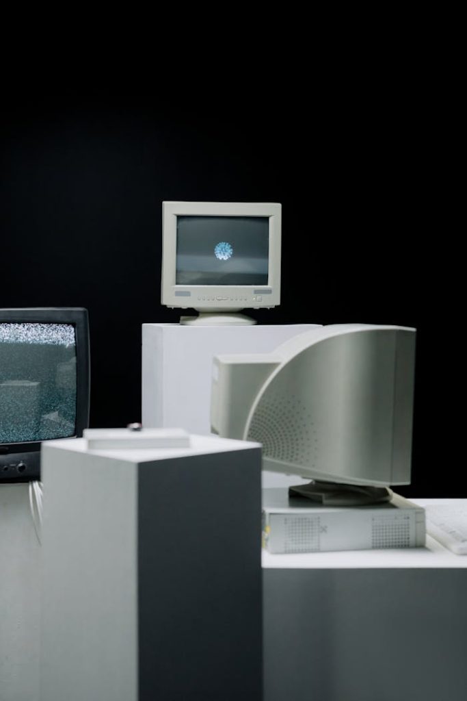 computer-monitors-on-white-table-8875501 Vintage computer monitors arranged in a minimalist setup with a dark background, showcasing technology evolution.
